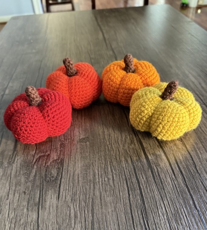 4 crocheted amigurumi pumpkins make with the 4 different combinations of yarn over and yarn under stitches made with red, orange, and yellow worsted weight yarn