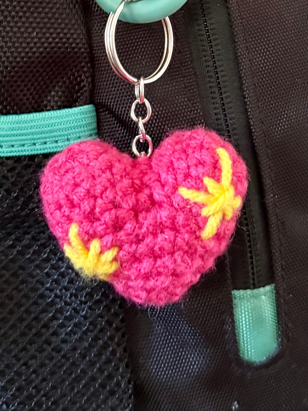 Close-up of a crocheted pink sparkle heart emoji keychain attached to a backpack, showing the finished project in use as a bag charm.