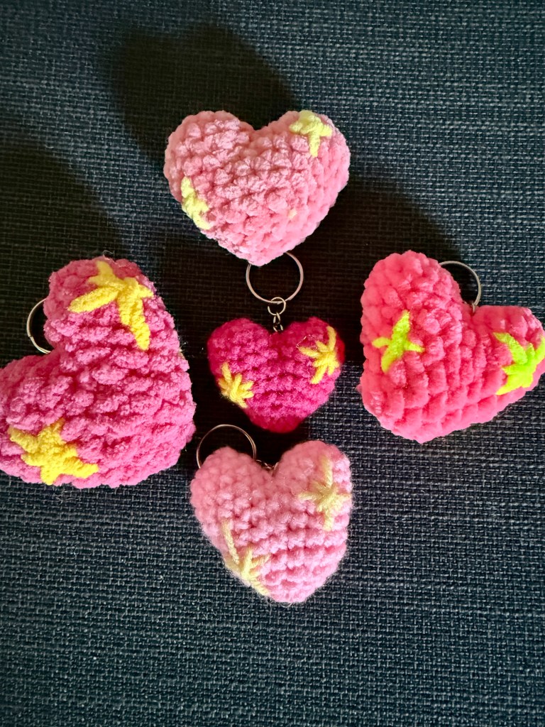 5 versions of the crocheted pink sparkle heart emoji keychain made with different yarns and different shades of pink and yellow