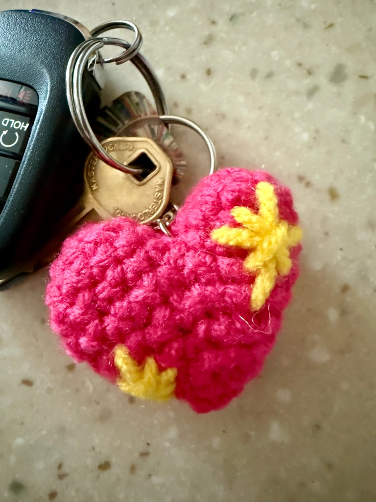 Close-up of a crocheted pink sparkle heart emoji attached to keys, showing the finished project in use as a keychain.