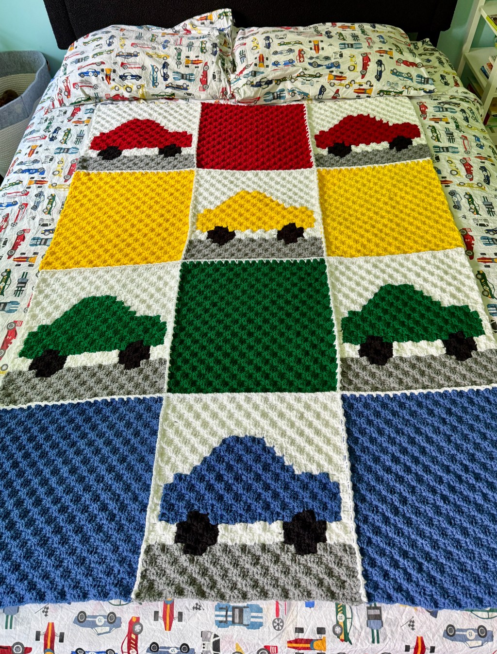 Colorful crochet blanket with red, yellow, green, and blue car squares spread across a bed with race-car sheets